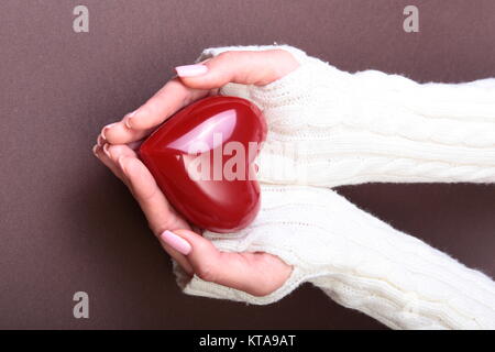 Weibliche Hände geben rotes Herz auf Gold Hintergrund isoliert, Weihnachten Winter Liebe Stockfoto