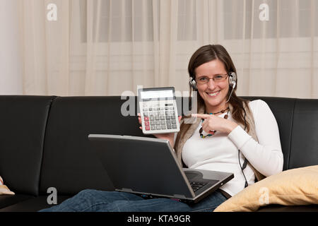 Intelligente Frau, die an einem Notebook arbeitet in ihrem Wohnzimmer und verwies auf die Taschenrechner Stockfoto