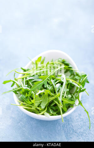 Frische Rucola Blätter in der Schüssel auf dem Tisch. Hellen Hintergrund, Nahaufnahme Stockfoto