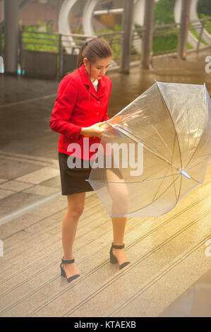 Thai hübsche Frau in Rot Bürosoftware Holding transparent Regenschirm zu Fuß auf Brücke über Sehenswürdigkeiten in Bangkok, Thailand. Stockfoto