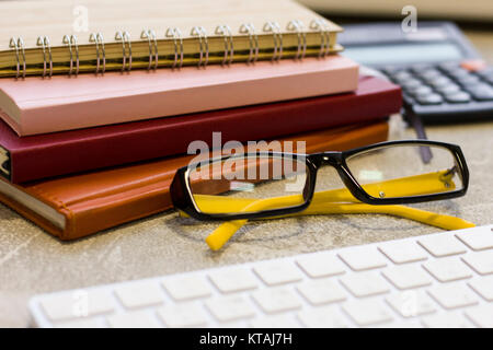 Ein Haufen von Notebooks und Planer, Gläser, eine Tastatur und einen Rechner an einem konkreten Hintergrund, aus der Nähe. Wirtschaft und Arbeit Konzept. Platz für Stockfoto