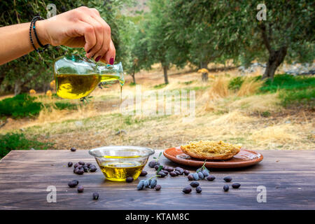 Flasche gießen kretische Olivenöl in einer Schüssel auf hölzernen Tisch in einen Olivenbaum Feld, Griechenland. Stockfoto