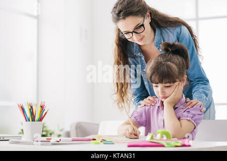 Mutter und Kind gemeinsam Hausaufgaben zu machen zu Hause, die Frau steht hinter das Mädchen und hilft ihr, Stockfoto