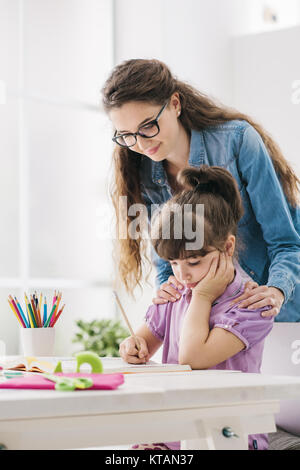 Mutter und Kind gemeinsam Hausaufgaben zu machen zu Hause, die Frau steht hinter das Mädchen und hilft ihr, Stockfoto