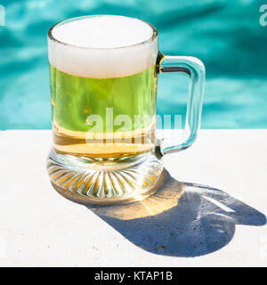 Tasse kaltes Bier auf der Seite des Pools Stockfoto