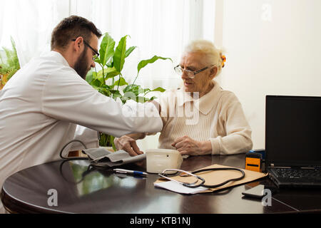 Eine private Arztpraxis. Geriatrischer Arzt nimmt den Blutdruck des Patienten auf. Stockfoto