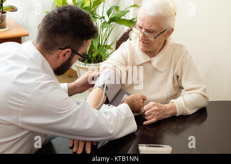 Eine private Arztpraxis. Geriatrischer Arzt nimmt den Blutdruck des Patienten auf. Stockfoto