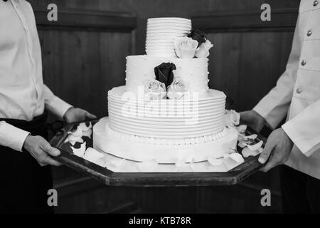 Multi Level weiße Hochzeitstorte auf einem Sockel und Blumen an der Spitze. Stockfoto