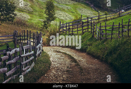 Unbefestigte Straße und rustikale Zäune in einem traditionellen siebenbürgischen Dorf, Brasov, Rumänien. Stockfoto