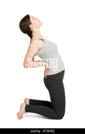 Seitliche Ganzkörper-Ansicht einer jungen Frau in weißen Hintergrund im Kniestand die Hände in die Hüften gestützt und den Oberkörper nach hinten beugend. Yoga-Position Ustrasana, das Kamel; in vereinfachter Variante. Stockfoto