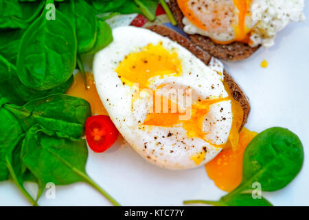 Leckere Eier Benedikt auf dem Sandwich mit Spinat und Cherry Tomaten auf dem weißen Teller, leckere Bio Ernährung, gesundes Essen Konzept Stockfoto