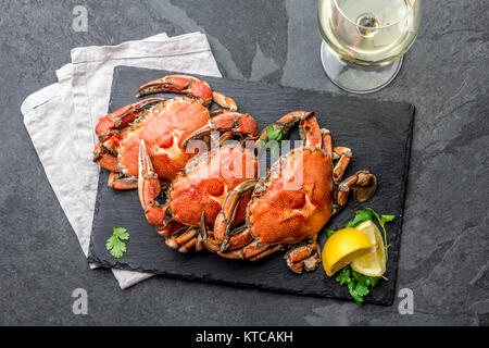 Gekochte Krabben auf dem schwarzen Schild mit weißem Wein serviert, schwarzer Schiefer Hintergrund, Ansicht von oben. Stockfoto