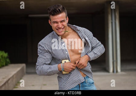 Stark und muskulös junger Mann auf der Straße. Er trägt ein T-Shirt mit braunen Streifen und tragen aufknöpfte. Stockfoto