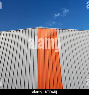 Ein grafischer orangefarbener Streifen auf einem modernen Gebäudedetail dagegen Ein blauer Himmel - geometrischer Minimalismus Stockfoto