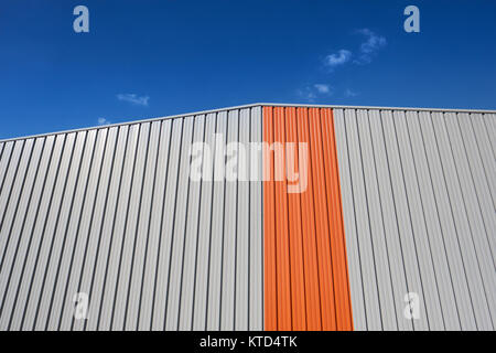 Ein grafischer orangefarbener Streifen auf einem modernen Gebäudedetail dagegen Ein blauer Himmel - geometrischer Minimalismus Stockfoto