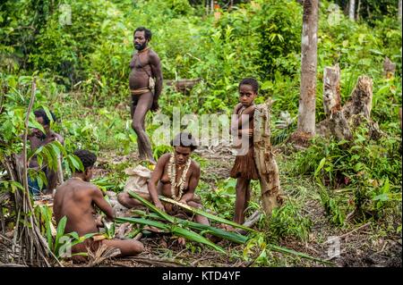 Die Leute vom Stamm der Korowai. Die Familie sitzt auf dem grünen Gras und macht ein Abendessen. Am 24. Juni 2012 in Onni Dorf, Neuguinea, Indonesien Stockfoto