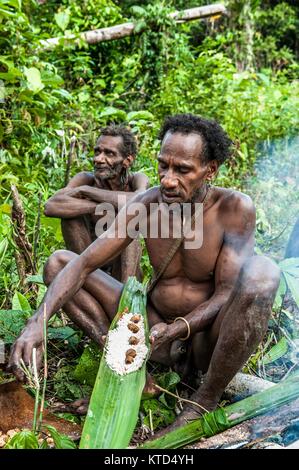 ONNI DORF, Neuguinea, Indonesien - Juni 24: Korowai Mann schlägt es gekocht sago Worms. Zeigt die Larven Würmer sago Palm. Korowai Stamm (Kombai, Kolufo Stockfoto