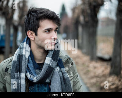 Hübscher junger Mann outdoor im Winter Mode, tragen dunkle Jacke und Wollschal im City Park Stockfoto