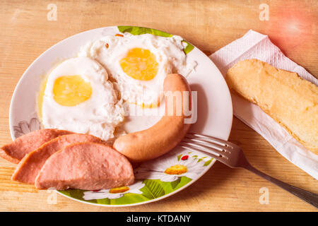 Gebratene Eier liegen in einer Platte. Sandwich und ein Würstchen auf einem Holz- Hintergrund. hausgemachte Speisen Stockfoto