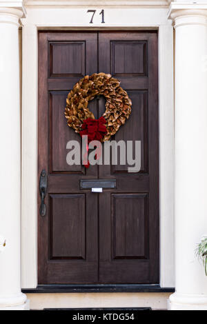 Ein Magnolia blatt Weihnachten Kranz hängt von einer hölzernen Tür in einem historischen Haus an der King Street in Charleston, SC. Stockfoto