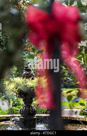 Ein Garten Springbrunnen umrahmt von Weihnachten ein Bug auf den schmiedeeisernen Zaun eines historischen Haus auf Legare Straße in Charleston, SC. Stockfoto