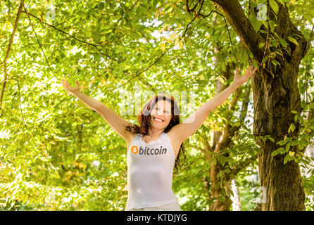 Glückliche Frau wirft die Arme in den Himmel, ein Garten, ein Tank Top mit der public domain bitcoin Logo, mit Freude leben das Leben mit der neuen curre Stockfoto
