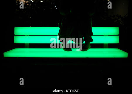 Die Beine ruhen auf der beleuchteten Bank während der Winter Lights Festival in Canary Wharf, London, Großbritannien Stockfoto