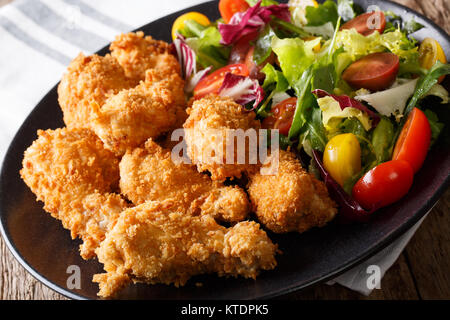 Würzige frittierte Hähnchenflügel in Semmelbrösel und frisches Gemüse Salat close-up auf einem Teller. Horizontale Stockfoto