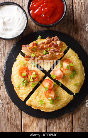 Kartoffelpuffer mit Speck, Tomaten, Zwiebeln und Saucen close-up auf einem Teller. Vertikal oben Blick von abovel Stockfoto