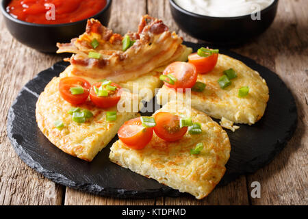 Leckere Kartoffelpuffer mit Speck, Tomaten, Zwiebeln und Saucen close-up auf dem Tisch. Horizontale Stockfoto