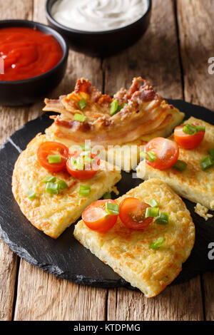 Kartoffelpuffer mit Speck, Tomaten, Zwiebeln und Saucen close-up auf einem Teller. Vertikale Stockfoto