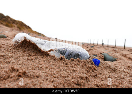 Abgebrochene Kunststoff Flasche Wasser am Strand links und bedeckt mit Sand