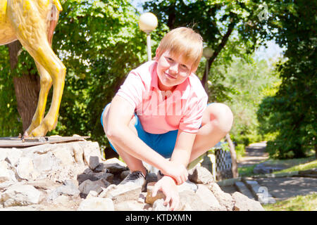 Lächelnde Junge in rosa Shirt hocken auf den Fersen Stockfoto