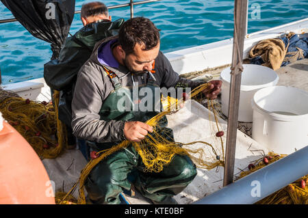 Katakolon, Griechenland - 31. Oktober 2017: die griechischen Fischer sammeln die Fische in die Netze nach Fischen in seinem Boot. Angeln in Holz- traditionelle Boote bleibt Stockfoto
