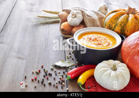 Pikante Kürbis, Karotten und Ingwer creme Suppe in eine dunkle Keramik Topf auf dem Holztisch, gewürzt mit Chili. Zutaten: Kürbis, Karotten, Stockfoto