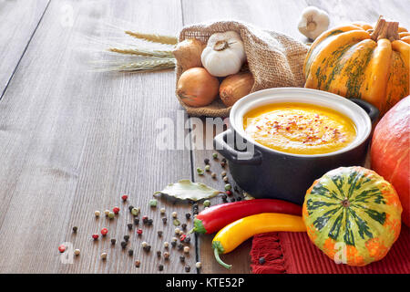 Pikante Kürbis, Karotten und Ingwer creme Suppe in eine dunkle Keramik Topf auf dem Holztisch, gewürzt mit Chili. Zutaten: Kürbis, Karotten, Stockfoto