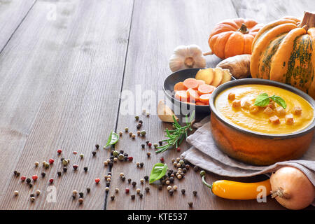 Kürbis creme Suppe mit Karotten und Ingwer in Keramik Schüssel auf Holz, gewürzt mit Croutons und Basilicum. Zutaten: Kürbis, Karotten, Ingwer, Zwiebel Stockfoto