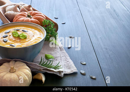 Pikante Kürbis creme Suppe mit Ingwer, Zwiebeln und Knoblauch in Keramik Schüssel auf den Holztisch. Die Suppe mit Kürbiskernen und Basilicum serviert. Raum Stockfoto