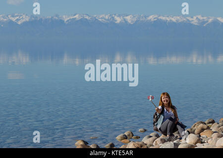 Ein weibliches Modell am Südufer von Issyk-Kol in Kirgisistan, im Hintergrund spiegeln sich die Berge des Nordufers. Stockfoto