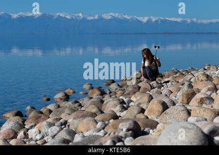 Ein weibliches Modell am Südufer von Issyk-Kol in Kirgisistan, im Hintergrund spiegeln sich die Berge des Nordufers. Stockfoto