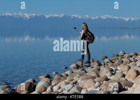 Ein weibliches Modell am Südufer von Issyk-Kol in Kirgisistan, im Hintergrund spiegeln sich die Berge des Nordufers. Stockfoto