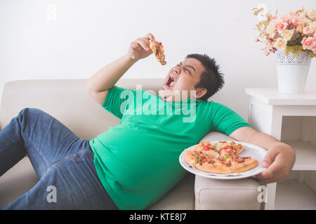 Faul übergewichtiger Mann essen Pizza bei der Verlegung auf einer Couch Stockfoto