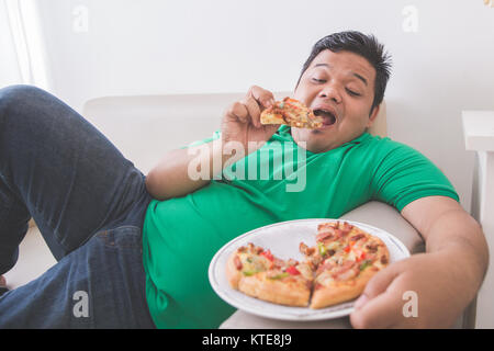 Faul übergewichtiger Mann essen Pizza bei der Verlegung auf einer Couch Stockfoto