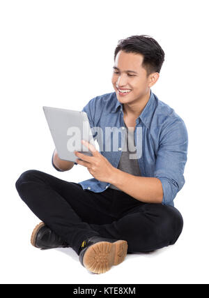 Junge asiatischer Mann mit Tablet-PC beim Sitzen auf dem Boden, isol Stockfoto