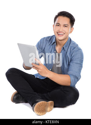 Junge asiatischer Mann mit Tablet-PC beim Sitzen auf dem Boden, isol Stockfoto
