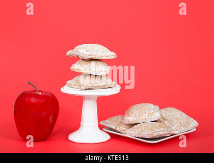 Miniatur square Apfelkuchen Knödel beschichtet mit Zucker, sitzen auf einem Sockel und einer quadratischen weißen Teller auf einem roten Hintergrund. Bright Red Apple sitzt n Stockfoto