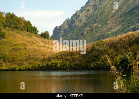 Ufer eines kleinen Bergsee vor dem Hintergrund einer unscharfen rocky mountain range an einem sonnigen Herbsttag Stockfoto