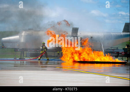 Ein Feuerwehrmann spritzt Wasser auf einer Flamme während einer Trainingseinheit auf einem Flughafen. Stockfoto