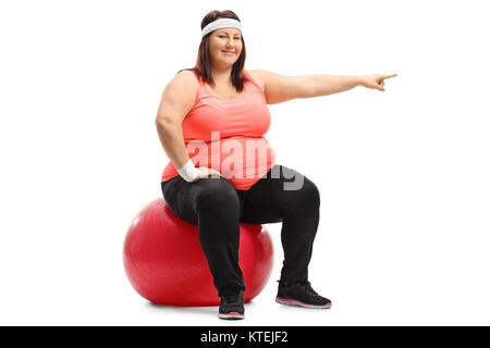 Übergewichtige Frau sitzt auf einem Pilates Ball und zeigen auf weißem Hintergrund Stockfoto