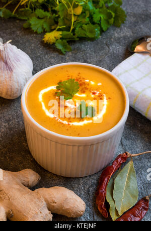 Gesunde reichhaltige vegetarische Kürbis Suppe am Tisch aus Stein durch frische Zutaten umgeben Stockfoto